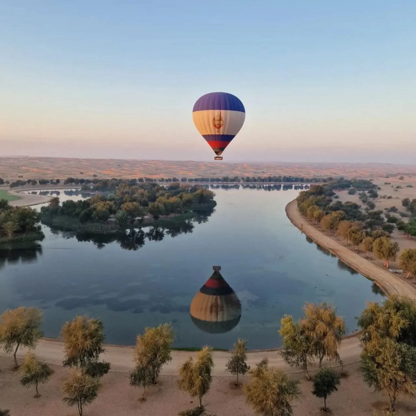 Hot air balloon flying over desert landscape and water at sunrise