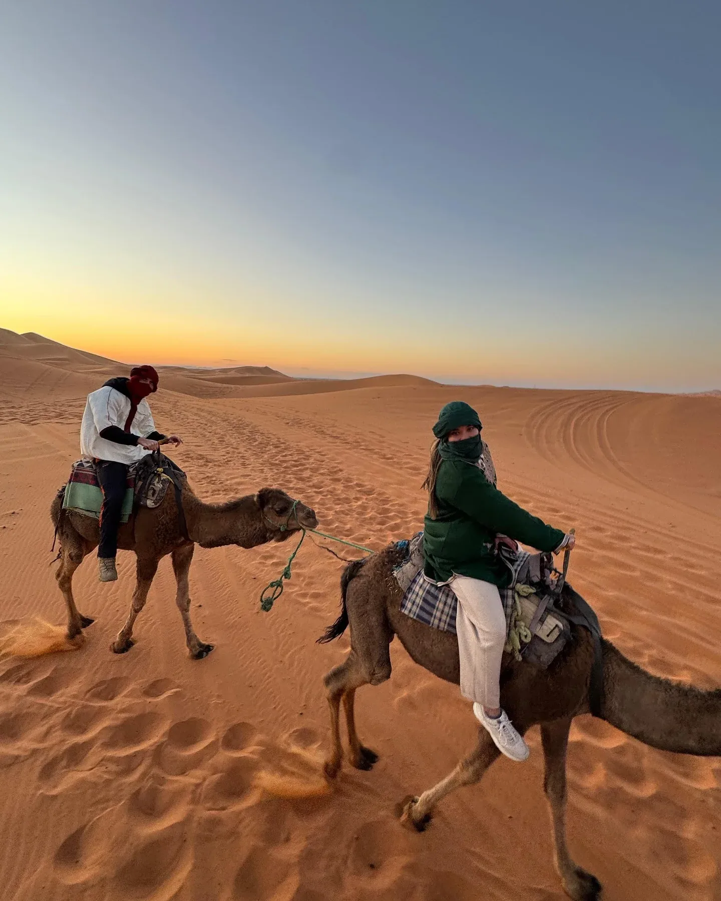 Tourists riding camels across Dubai desert dunes at sunset