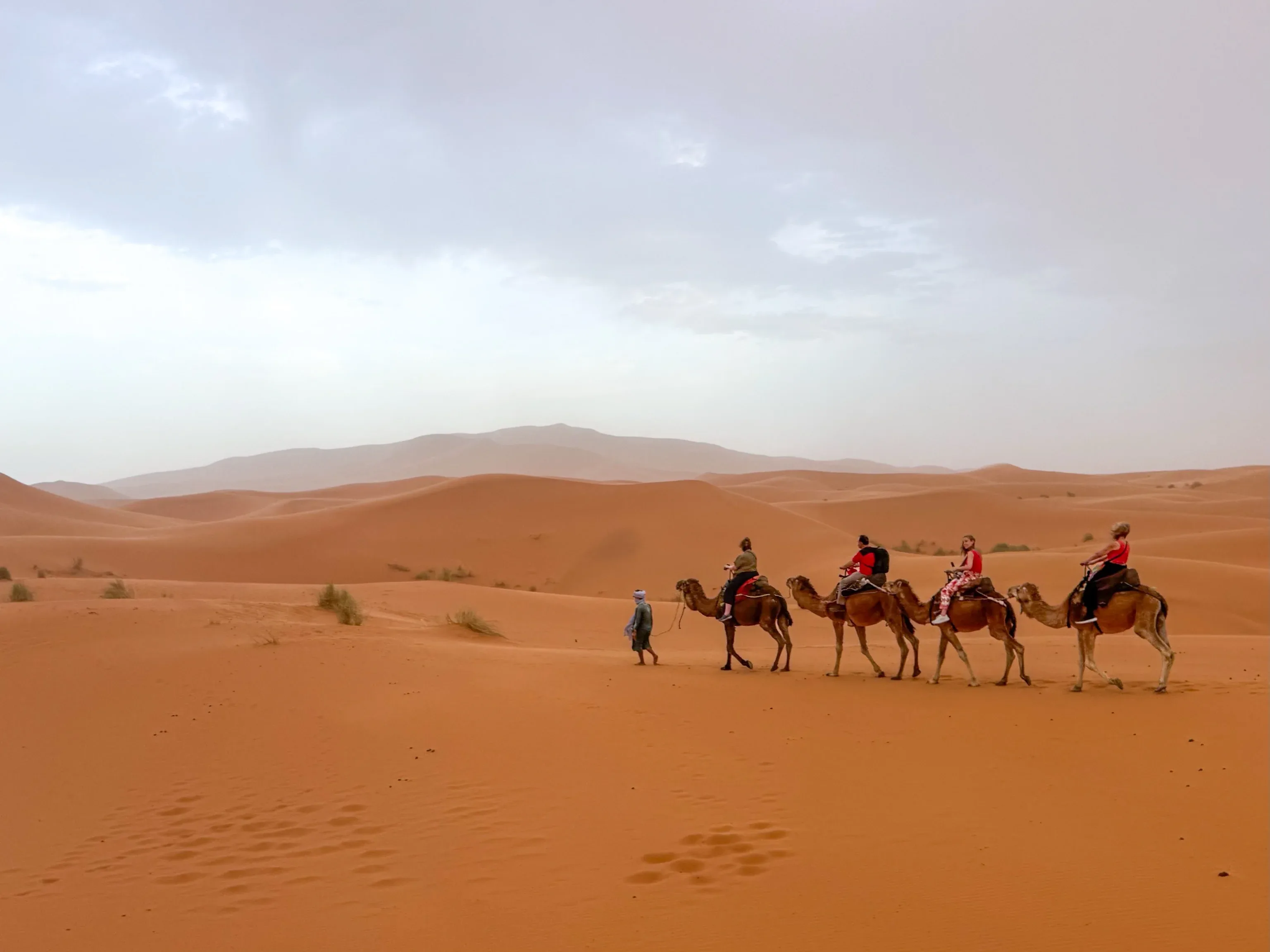 Tourists enjoying camel riding across Dubai desert dunes