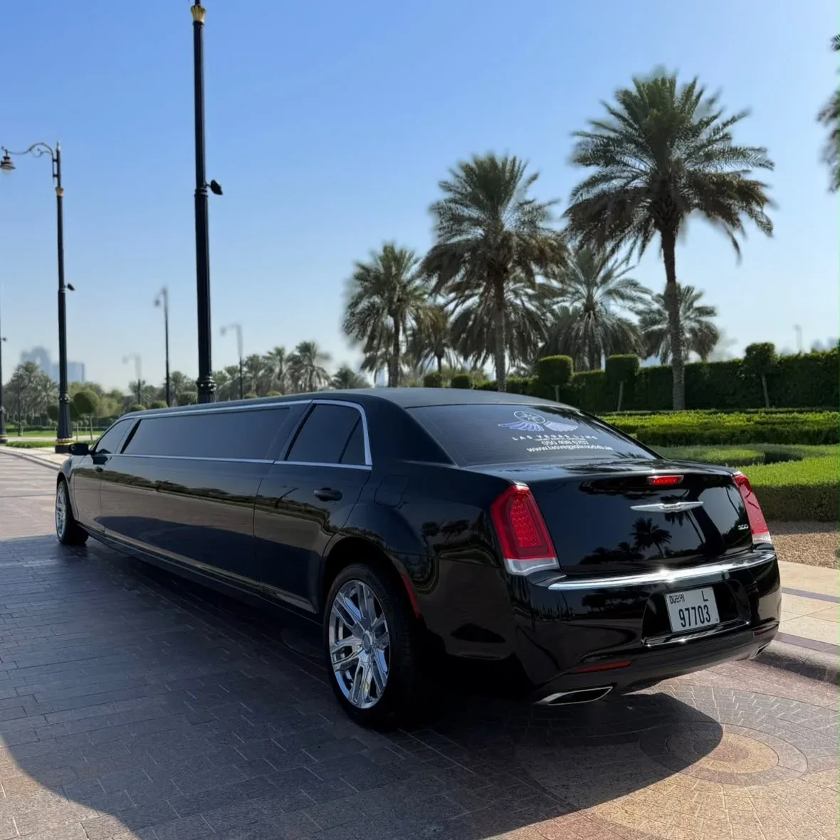 Black stretch limousine driving through a palm-lined Dubai setting