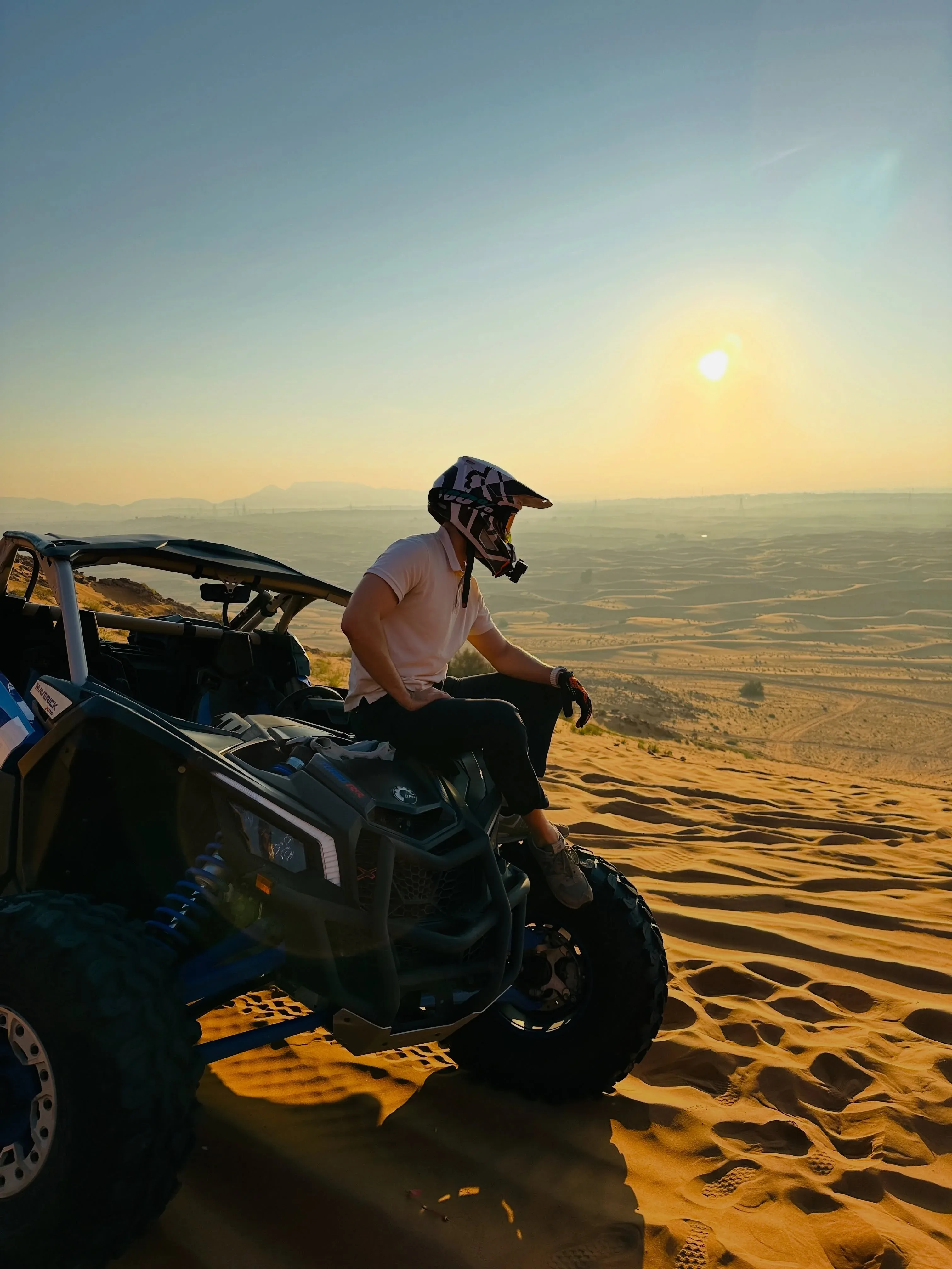 Can-Am Maverick buggy driving across Dubai desert dunes at sunset